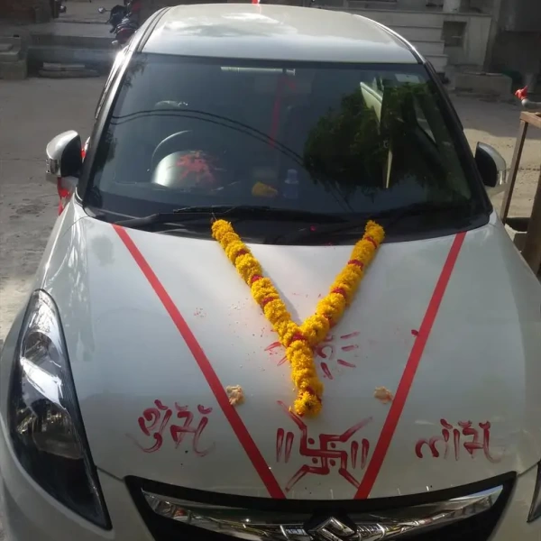White car decorated with marigold garlands, red ribbons, and Hindu symbols for new-vehicle puja.