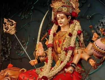 Bejeweled goddess seated on tiger, garlanded, holding trident, sword, and lotus, blessing devotees.