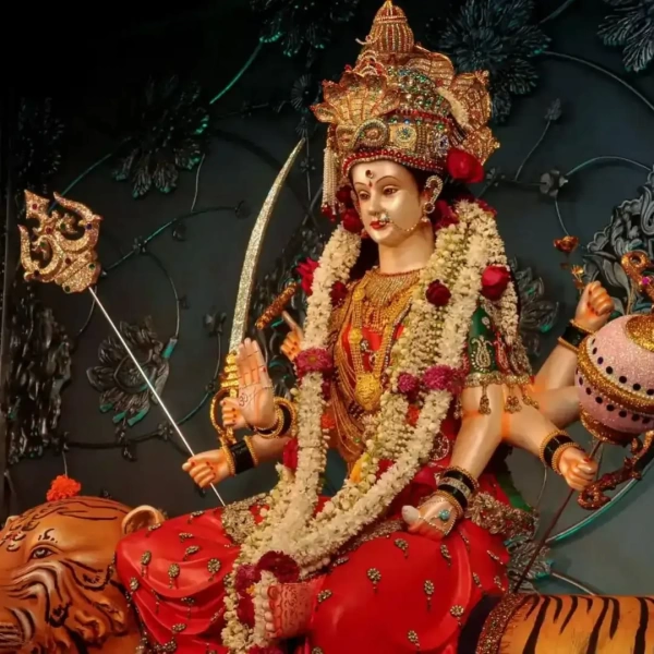 Bejeweled goddess seated on tiger, garlanded, holding trident, sword, and lotus, blessing devotees.