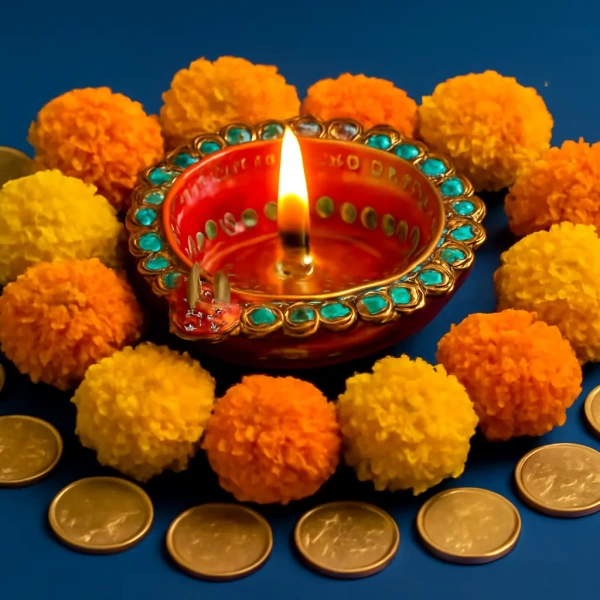 Lit red diya surrounded by turquoise-studded rim, marigold pom-poms, and arranged coins symbolizing Dhanteras prosperity.