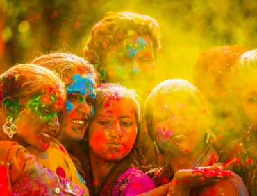 Friends joyfully celebrate with vibrant colored powder clouds during Holi, smiling together amid golden haze.