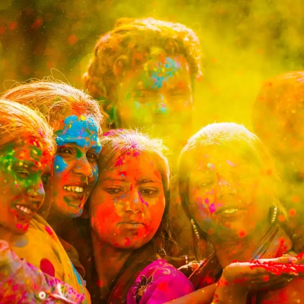 Friends joyfully celebrate with vibrant colored powder clouds during Holi, smiling together amid golden haze.