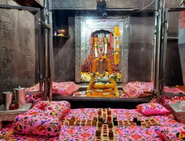 Sacred Omkareshwar Jyotirlinga sanctum with Shiva lingam, marigold garlands, silver vessels, embroidered pink cushions.