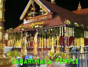 Night view of decorated Sabarimala Ayyappa temple with garlands, gold-plated roof, illuminated pillars, and pilgrims outside.