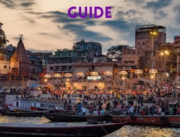 Evening view of Varanasi ghats with illuminated temples, crowded steps, and boats on the Ganges.